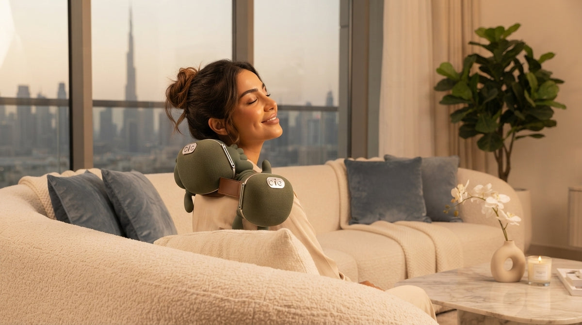 A woman relaxing on a sofa at home using a cordless neck and shoulder massager to relieve tension.
